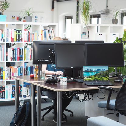 Arbeitsbereich bei e-pixler mit mehreren Monitoren und Regalen voller Bücher.